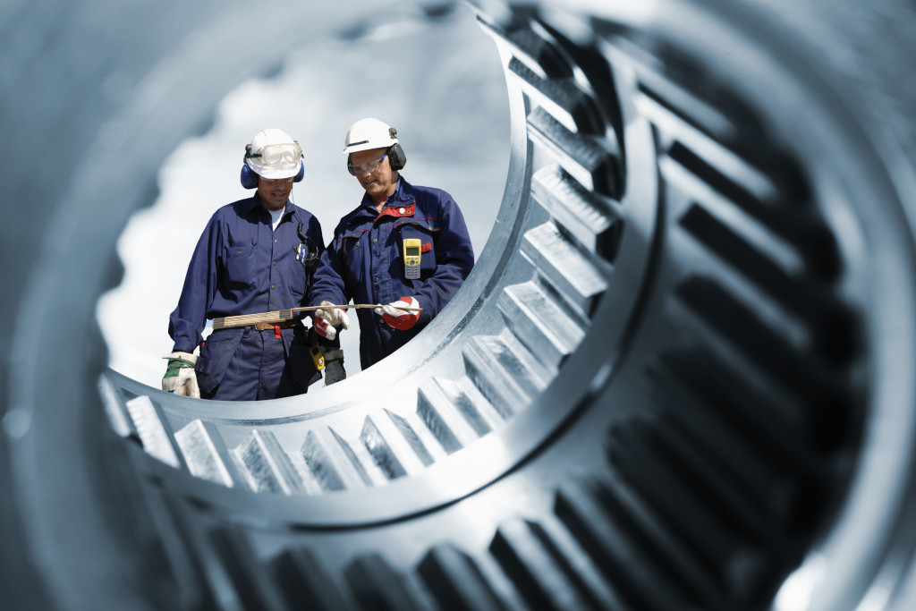 close up picture of a gear with 2 men at work